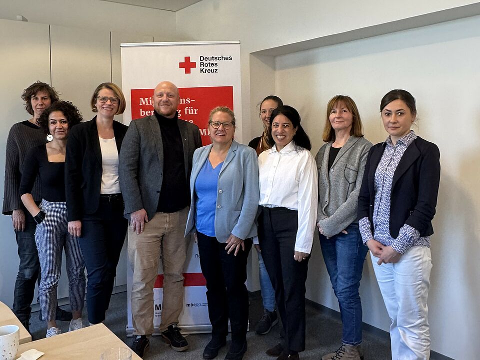 Gruppenbild von acht Personen vor einem MBE-Aufsteller des DRK