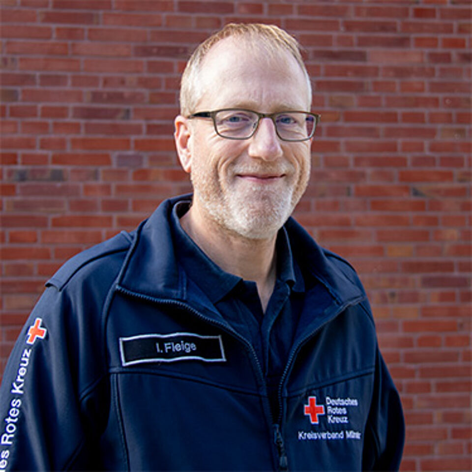 Mann mit Brille in blauer DRK-Jacke vor Backstein-Hintergrund