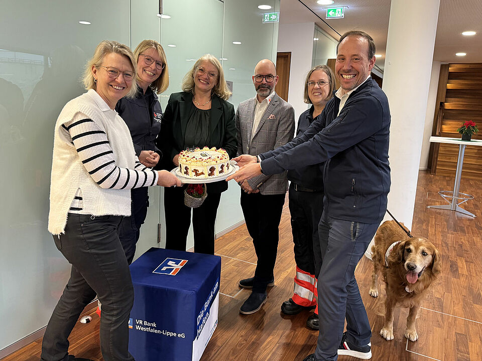 Kuchen Sechs Personen stehen in einem Halbkreis und halten einen Kuchen in die Kamera
