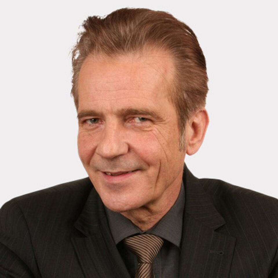 Mann mit dunklem Hemd, Sakko und gemusterter Krawatte vor weißem Hintergrund