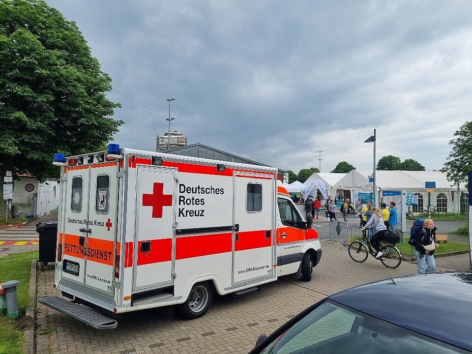 Rettungsmittel Special Olympics Ein Krankentransportwagen auf einem Veranstaltungsgelände, im Hintergrund sind Zelte und Besucher*innen zu sehen