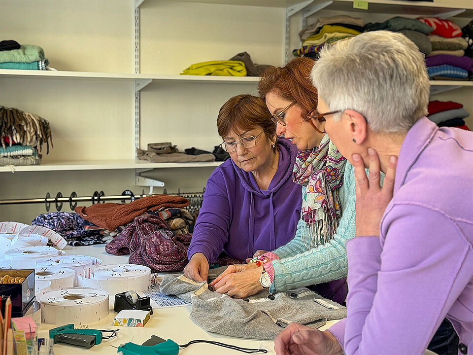 Kleidersortierung 3 Frauen sortieren gemeinsam Kleiderspenden