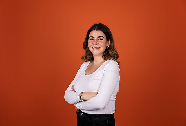 Junge Frau mit braunen Haaren vor orangenem Hintergrund