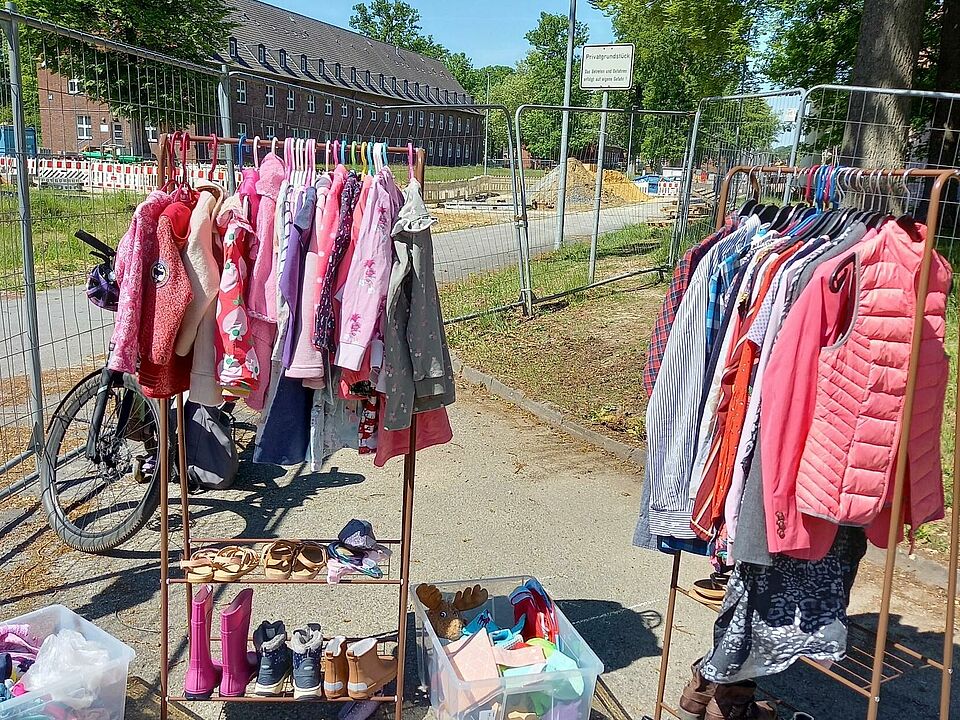 Zwei Kleiderstangen mit bunter Kinderkleidung, darunter stehen Schuhe