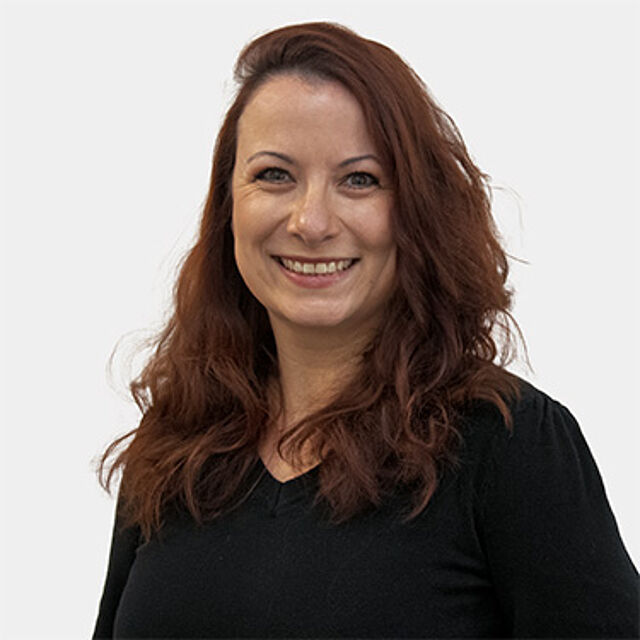 Eine Frau mit rot-braunen langen Haaren, die eine schwarze Bluse trägt.