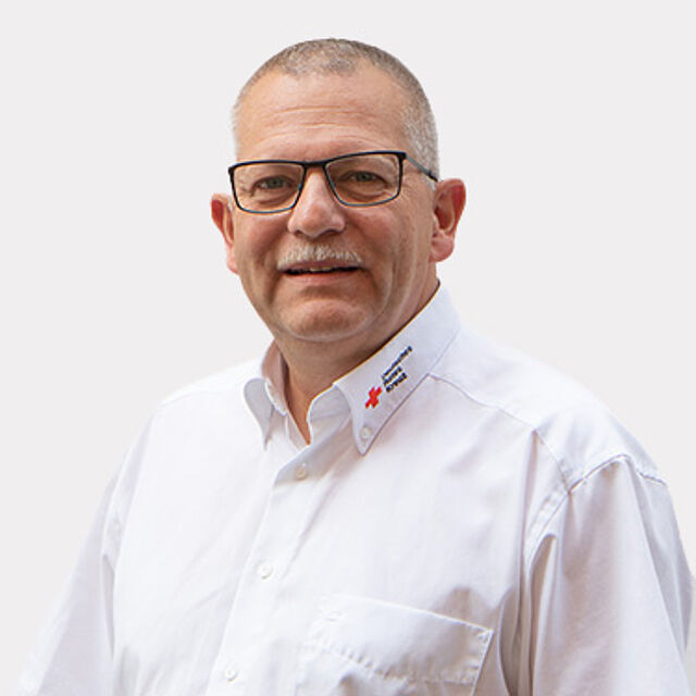 Mann mit Brille und weißem DRK-Hemd vor weißem Hintergrund