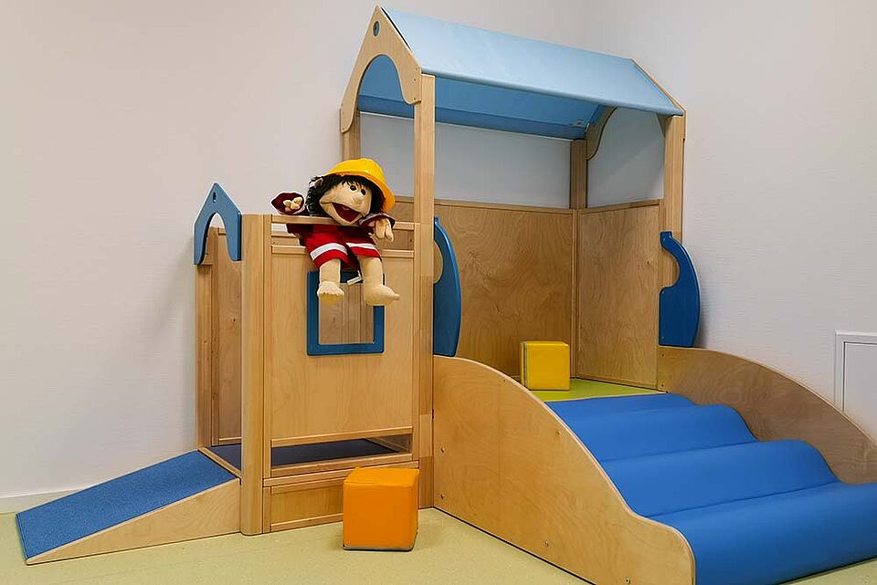 Eine kleine Kletterburg in einem weißen Raum mit Spielmaterialen und einer Puppe