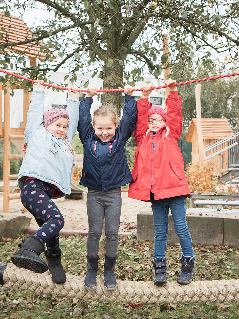 Drei Kinder hängen auf einem Outdoor-Spielplatz an einem Seil