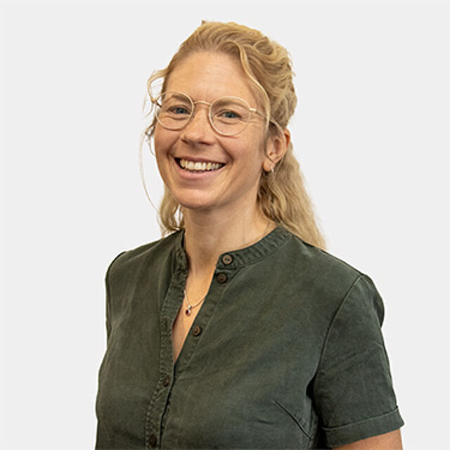 Eine Frau mit blonden Locken und Brille in einem grünen Hemd.