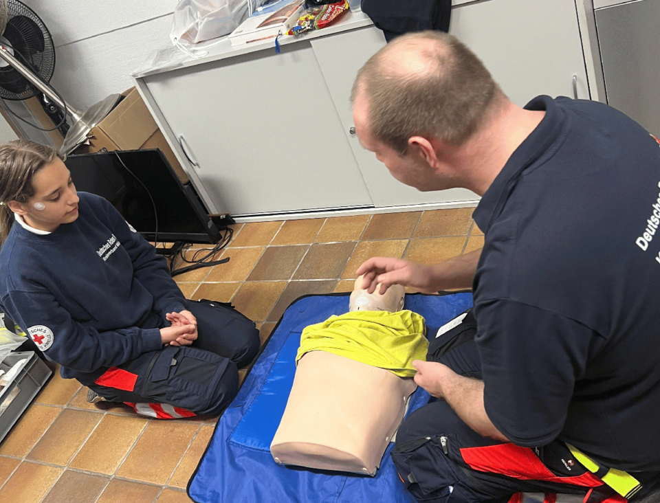 Reanimationspuppe Ein Mann und ein Mädchen in Einsatzkleidung knien vor einer Reanimationspuppe