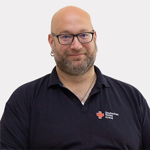 Mann mit Brille und einem blauen DRK-Poloshirt vor weißem Hintergrund