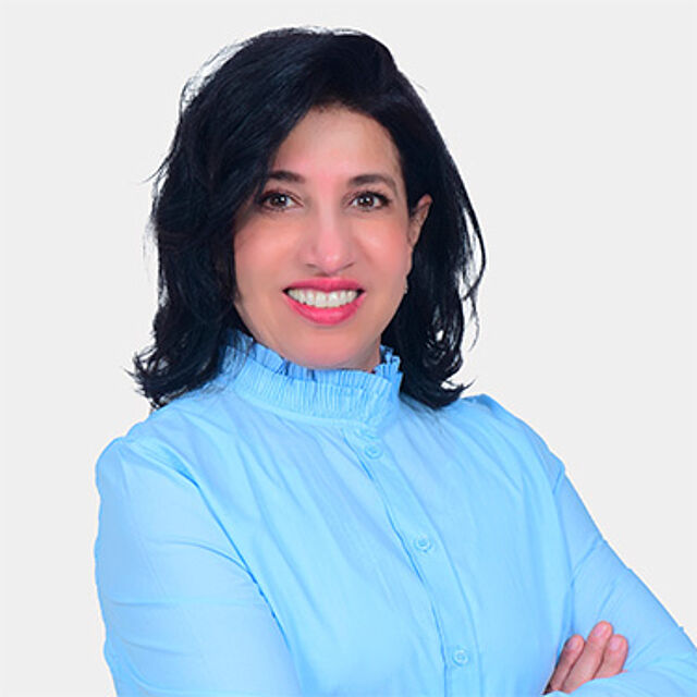 Frau mit schwarzen Haaren und blauer Bluse vor weißem Hintergrund