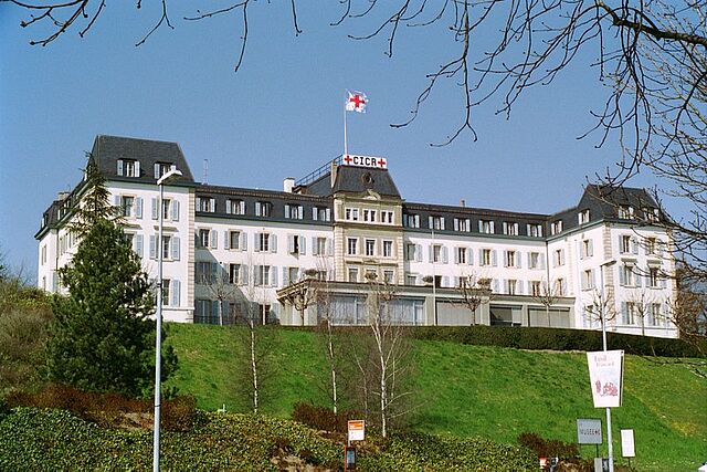 Zu sehen ist ein weißes, schmuckvolles Gebäude mit gehisster DRK-Fahne und einem Banner mit roten Kreuzen und "CICR"