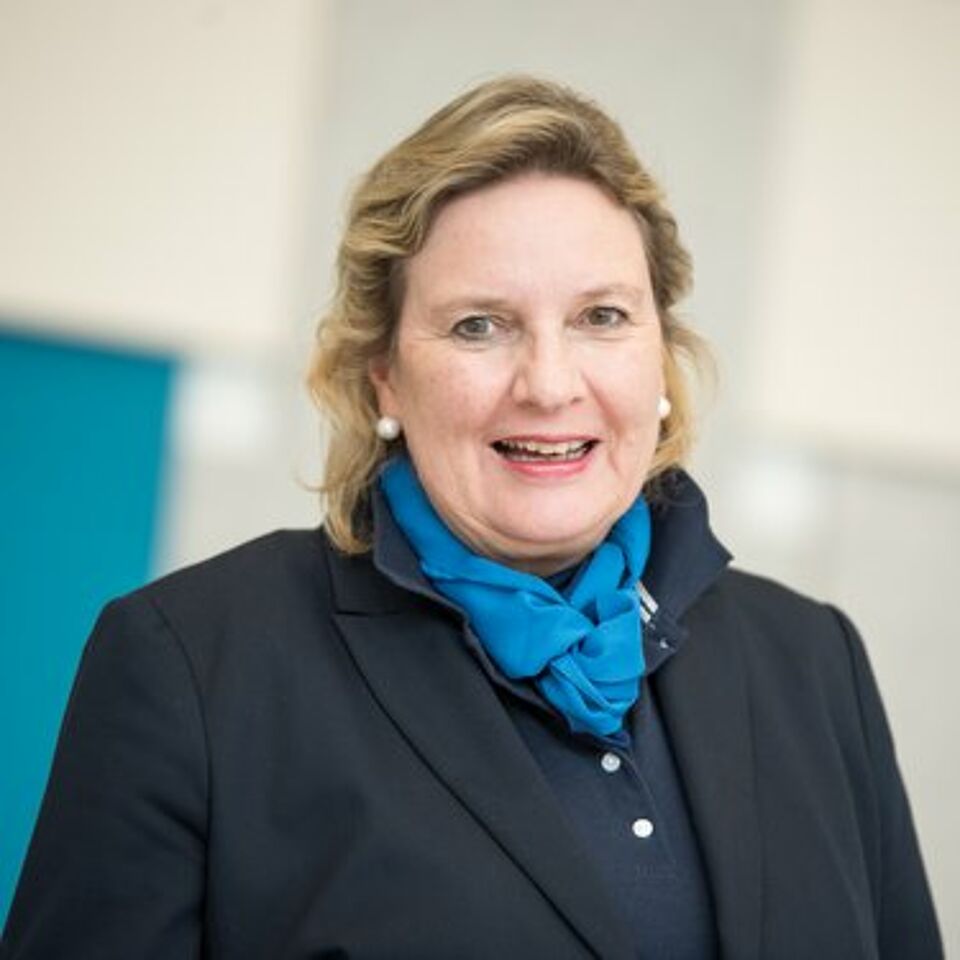 Frau mit blonden Haaren, blauem Schal und schwarzem Blazer