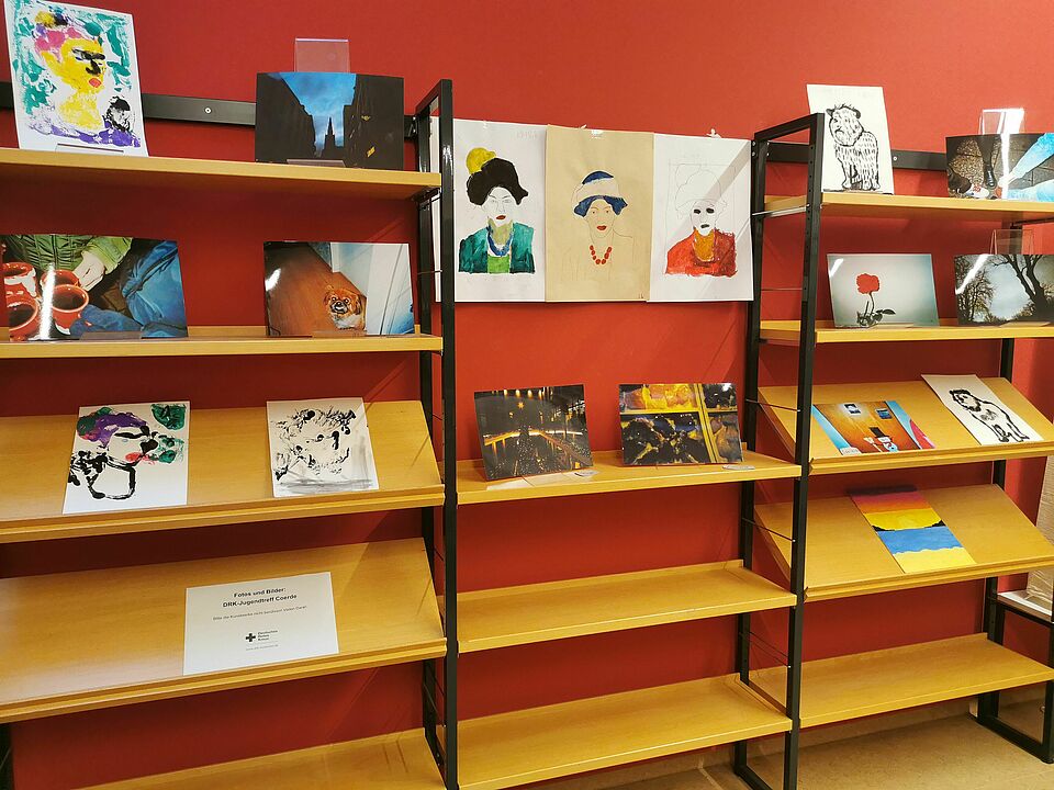 Ausstellung Jugendtreff Holzregale, auf denen Bilder liegen, vor einer roten Wand