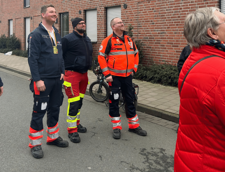 Drei Personen in Einsatzkleidung stehen auf der Straße und schauen nach oben.