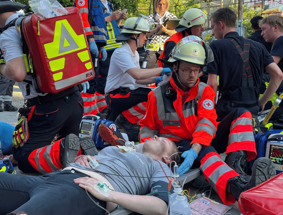 Viele Personen auf dem Boden. Einsatzkräfte kümmern sich um Verletzte, viel medizinisches Equipment ist zu sehen.