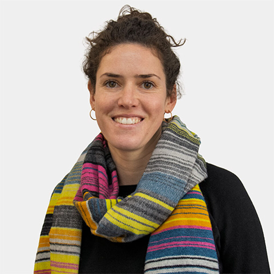 Frau mit braunen Haaren, buntem Schal und schwarzem Oberteil vor weißem Hintergrund