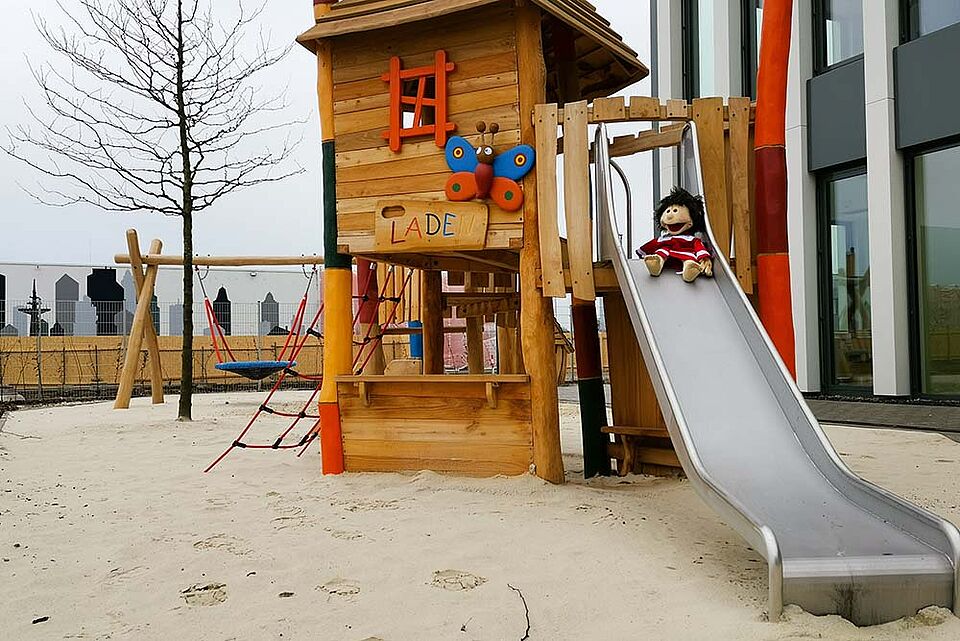 Ein Klettergerüst aus Holz und mit Rutsche neben einem modernen Gebäude