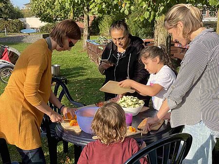 Mehrere Personen stehen um einen Tisch herum und schneiden Gemüse
