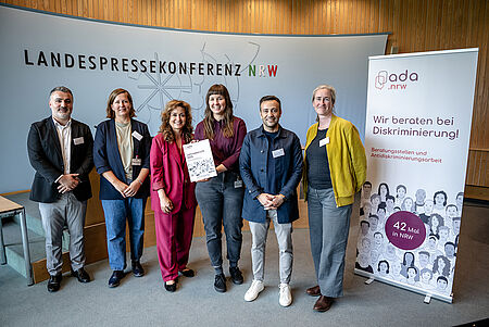 6 Personen stehen vor einem Podium