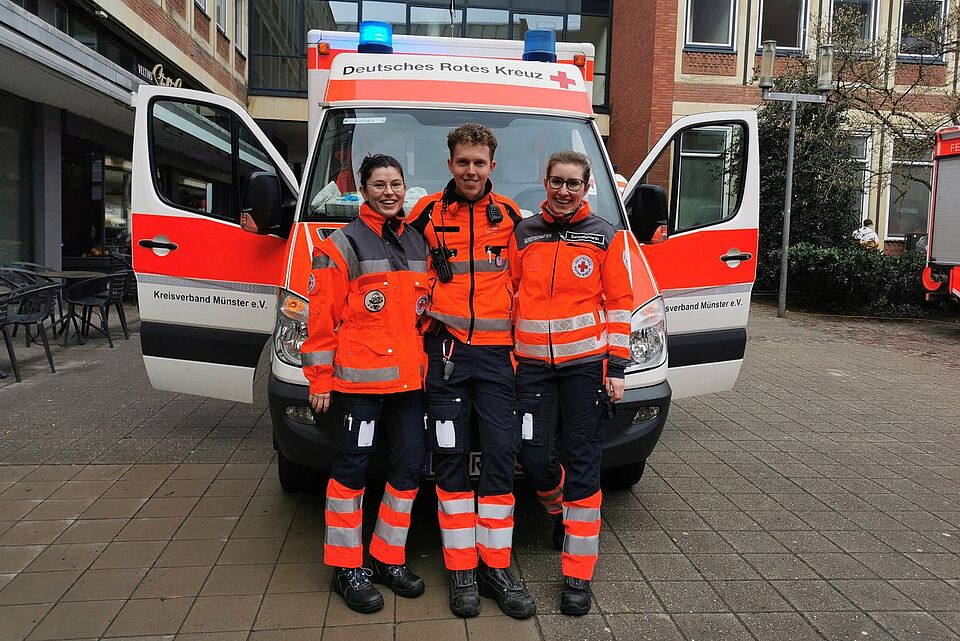 Rosenmontag Drei Personen in Einsatzkleidung vor einem RTW mit offenen Türen und Blaulicht