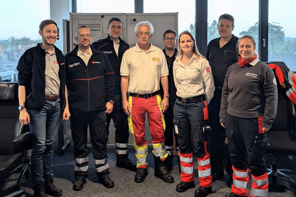 Giro Eine Gruppe von Personen in Einsatzkleidung von verschiedenen Hilfsorganisationen vor einer Stellwand.