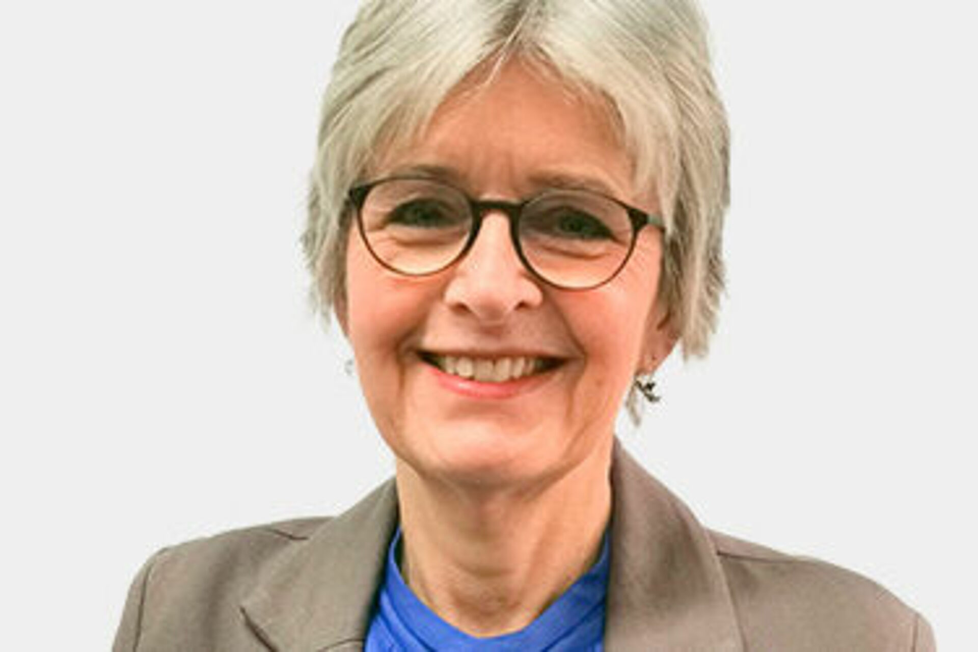 Frau mit weißen kurzen Haaren, Brille, blauer Bluse und grauem Blazer vor weißem Hintergrund