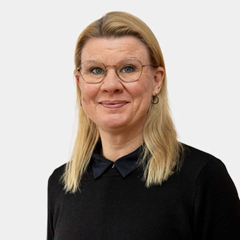 Frau mit blonden Haaren, Brille und schwarzem Oberteil vor weißem Hintergrund