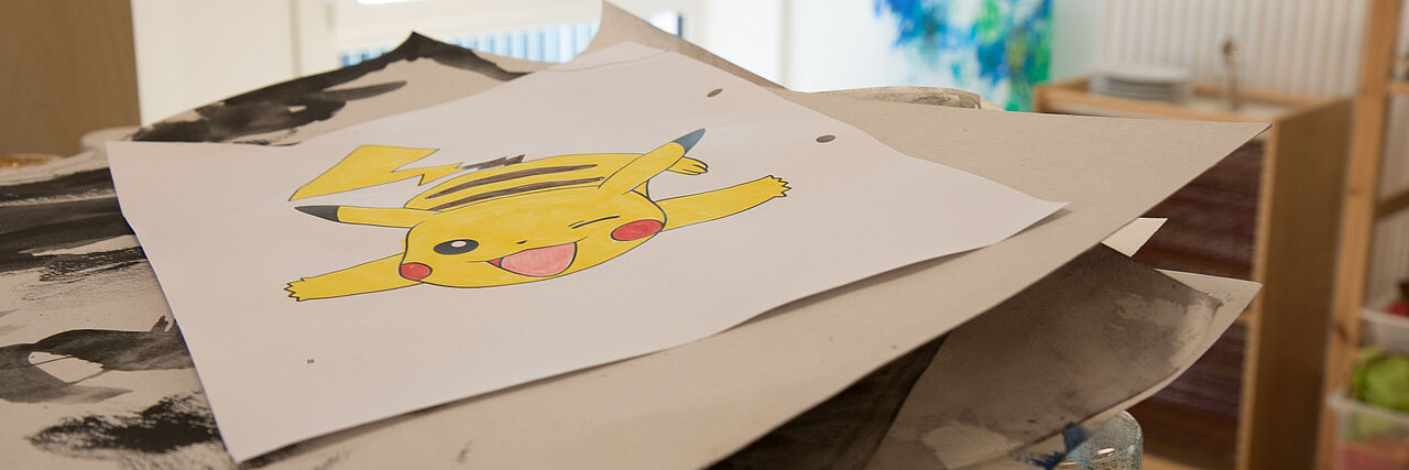 Schatzkiste Ein Blatt mit einer Zeichnung von einem gelben Pikachu liegt auf einem Stapel Pappe